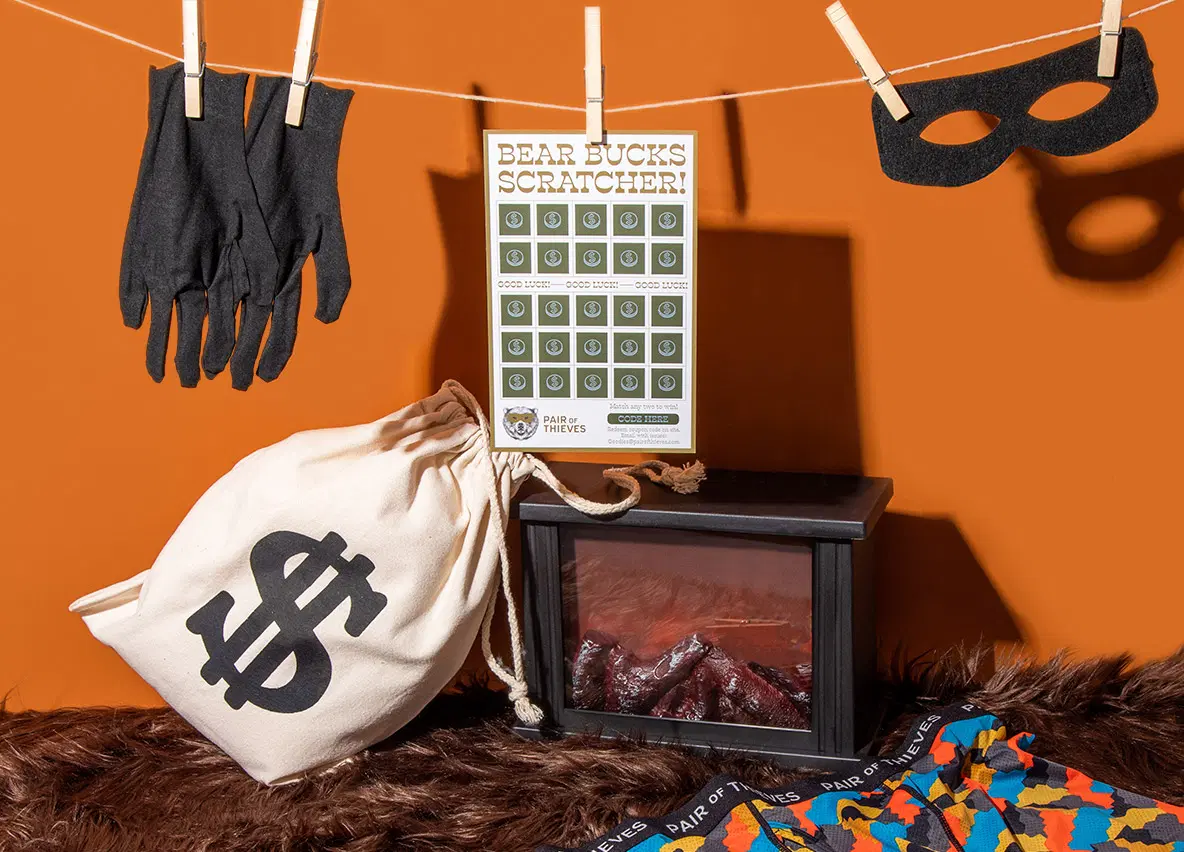 Pair of Thieves Bear Bucks Scratcher hanging from a clothesline with a money bag and mask